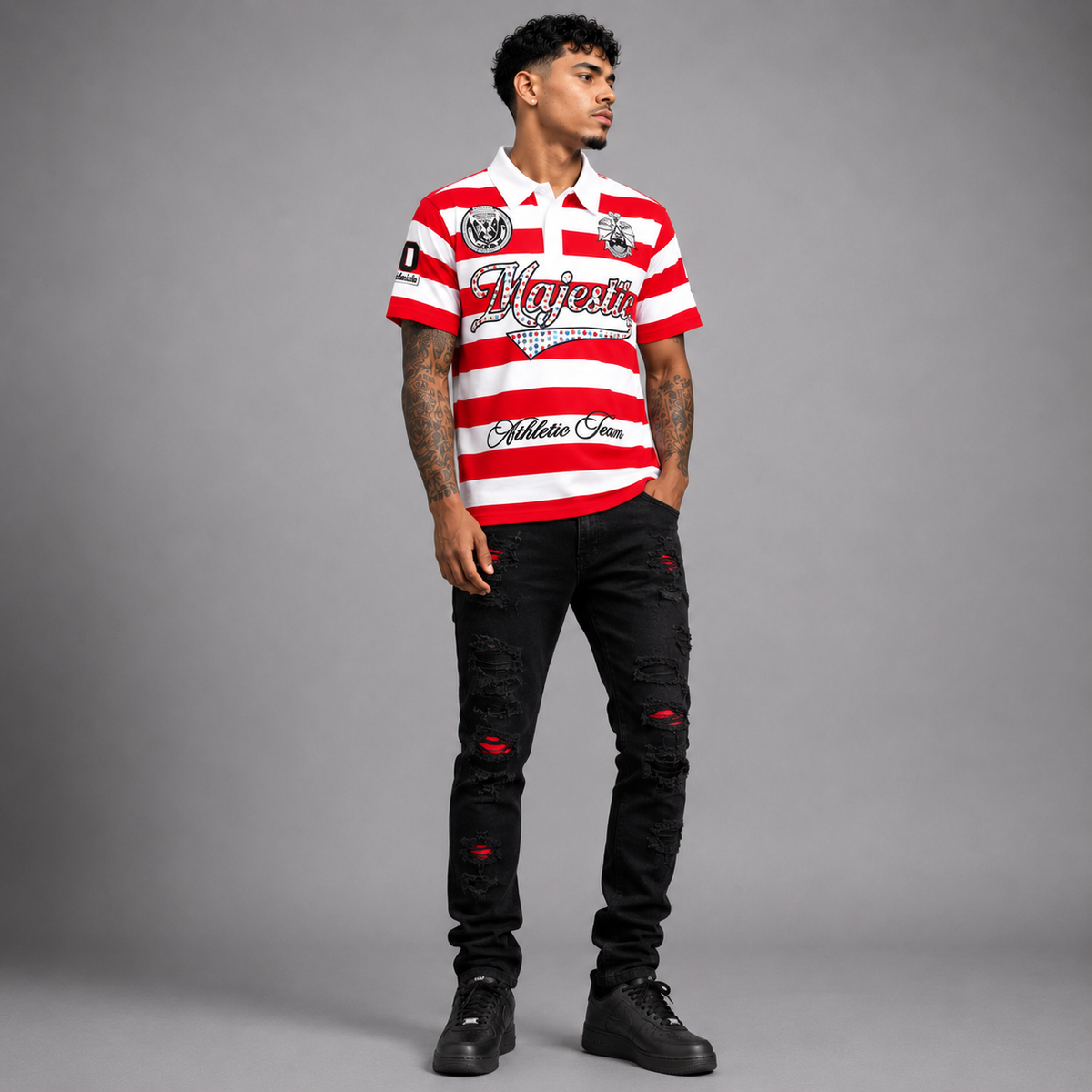 A man modeling a red and white horizontally striped short-sleeve polo shirt with 'Majestic' and 'Athletic Jeans' branding, paired with black distressed jeans and black sneakers, against a solid gray studio background.