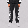 A person wearing black acid-wash sweatpants with bold white flame graphics down the sides, paired with a matching black hoodie and white sneakers, shown from the waist down against a light gray studio background.