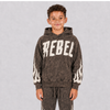 A young boy wearing a dark brown acid-wash hoodie with 'REBEL' printed in distressed white letters across the chest and white flame graphics on the sleeves, paired with matching acid-wash sweatpants, set against a plain gray studio background.