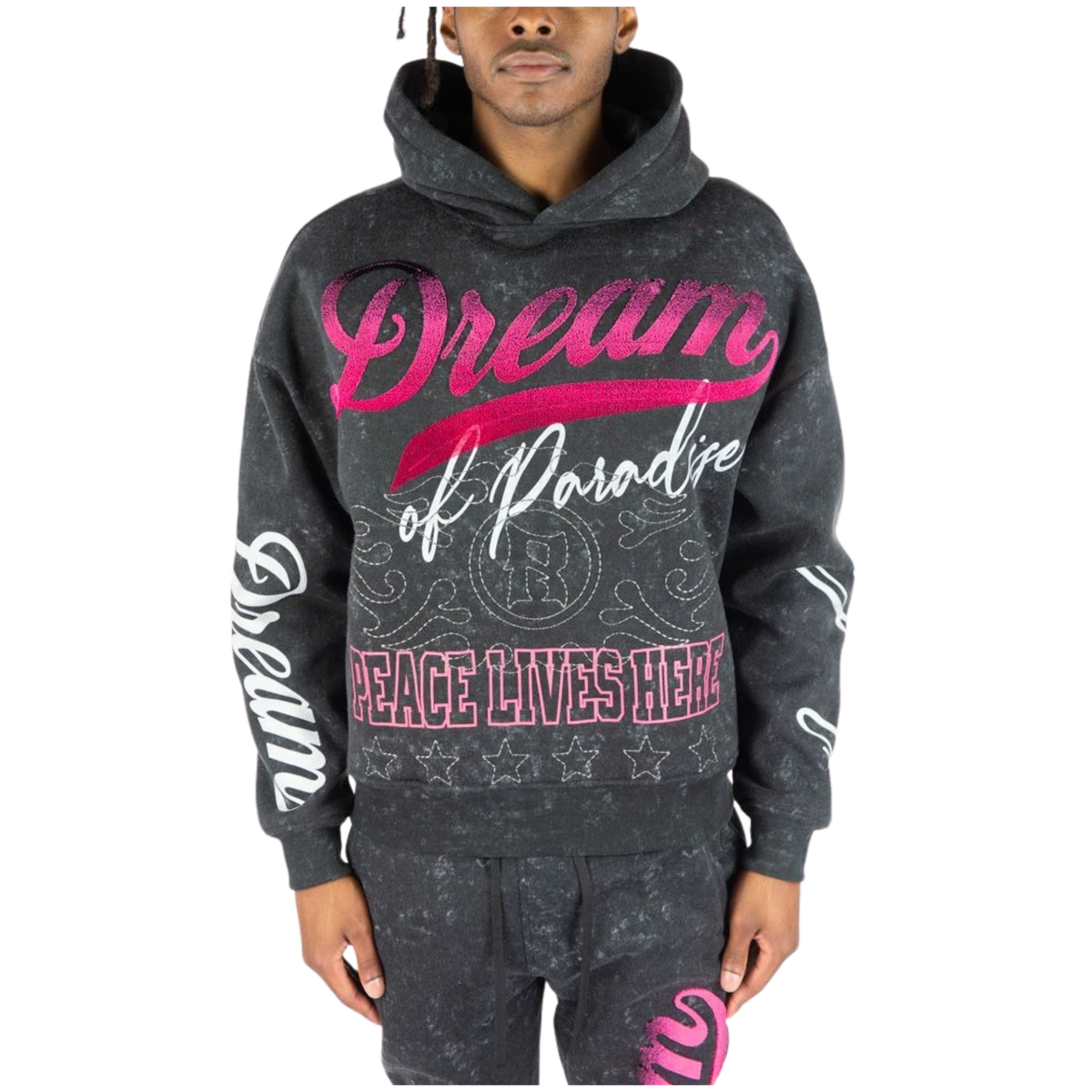 A man wearing a dark black acid-wash hoodie with pink and white graphic text reading 'Dream of Paradise' and 'PEACE LIVES HERE', paired with matching dark gray sweatpants against a white background.