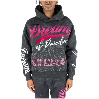 A man wearing a dark black acid-wash hoodie with pink and white graphic text reading 'Dream of Paradise' and 'PEACE LIVES HERE', paired with matching dark gray sweatpants against a white background.
